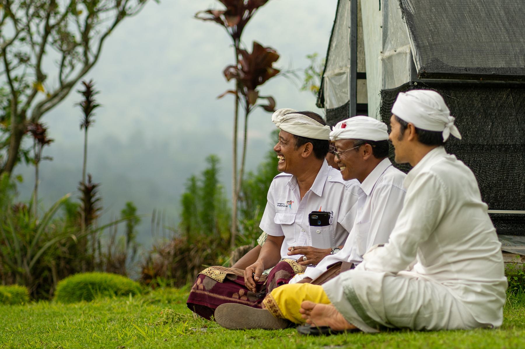 3 mens sitting criss cross on green grass wearing white