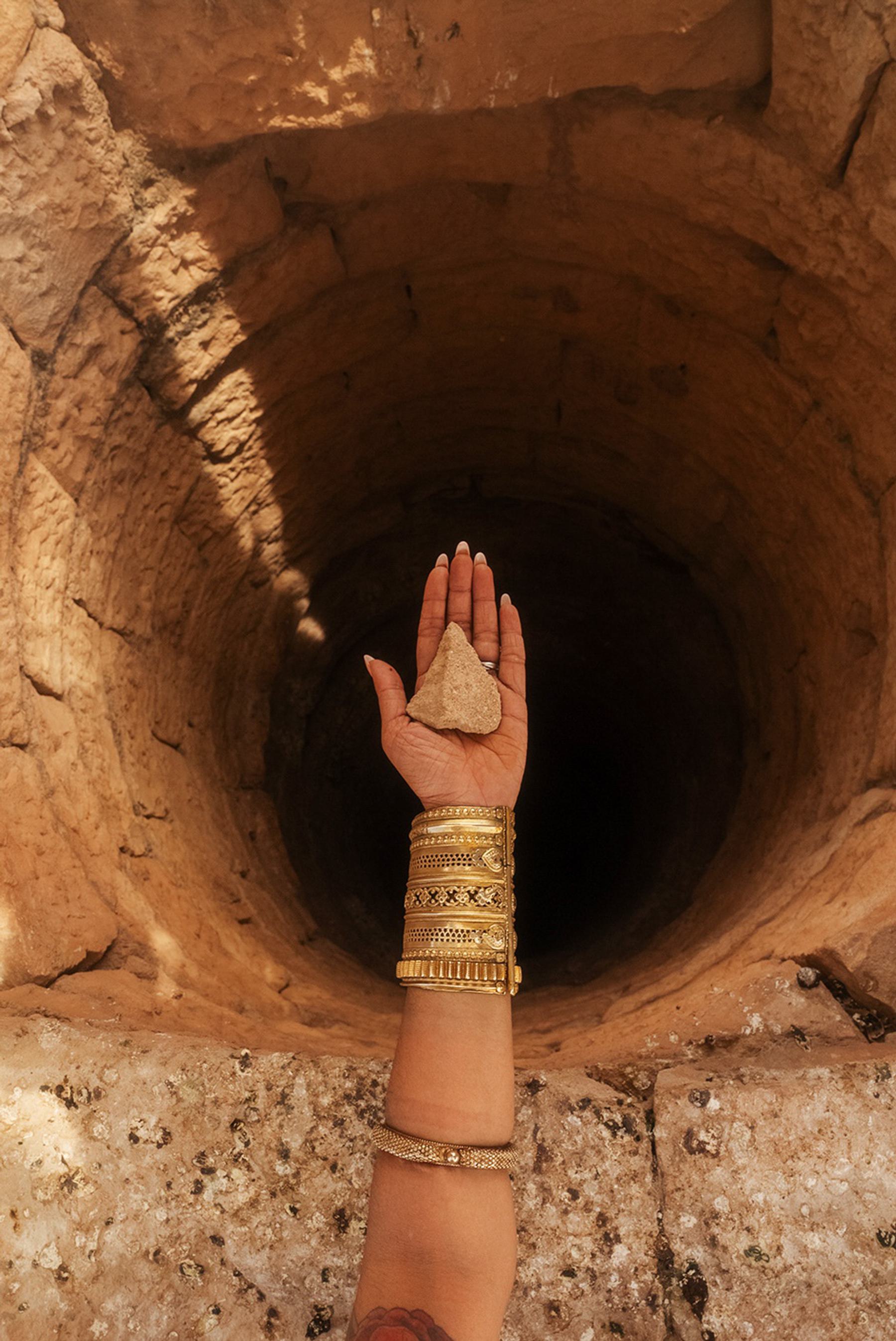 a female hand wearing a golden bracelet is stretched our in front of a very deep well