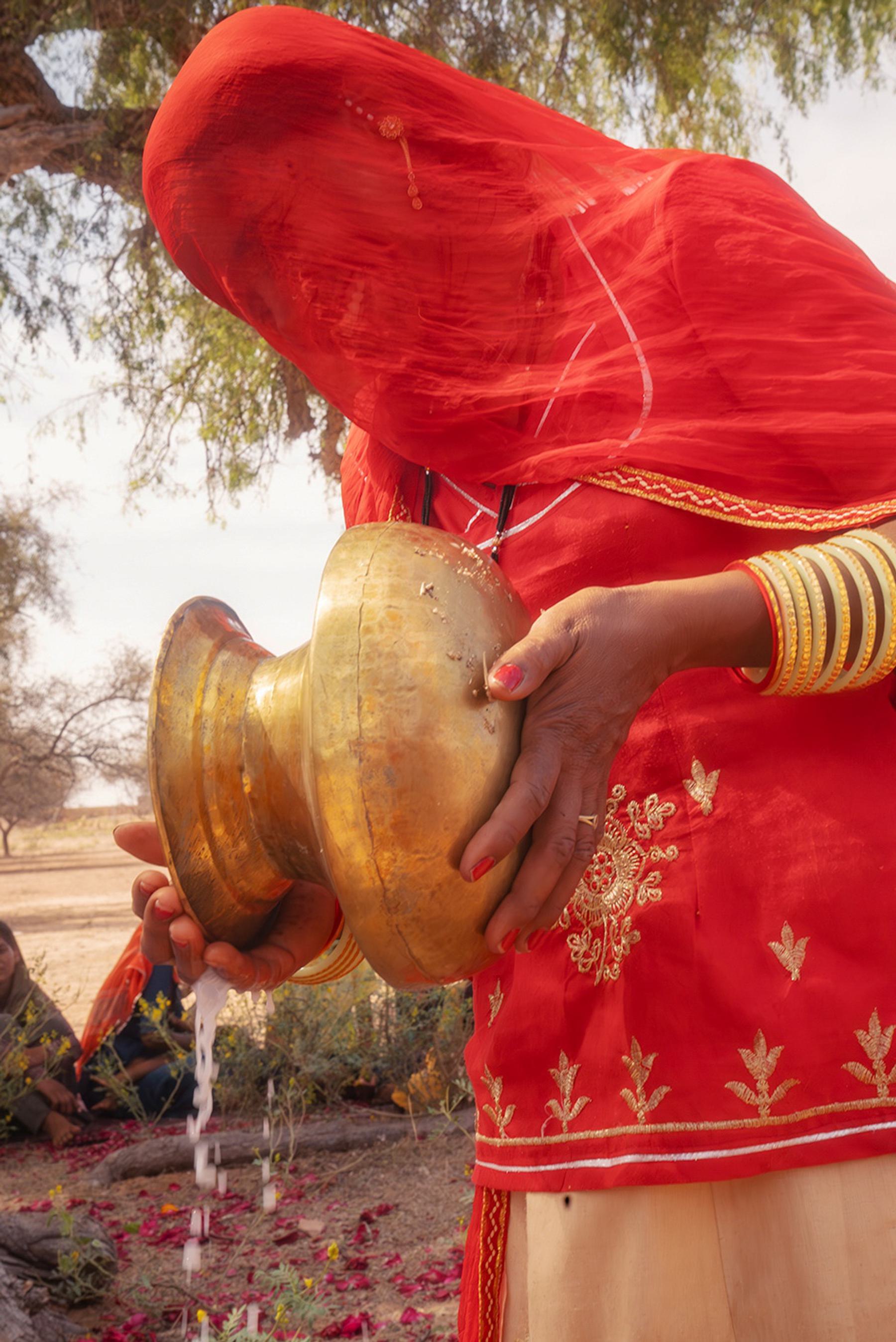 a woman dressed in red with her face covered pours water from a vase