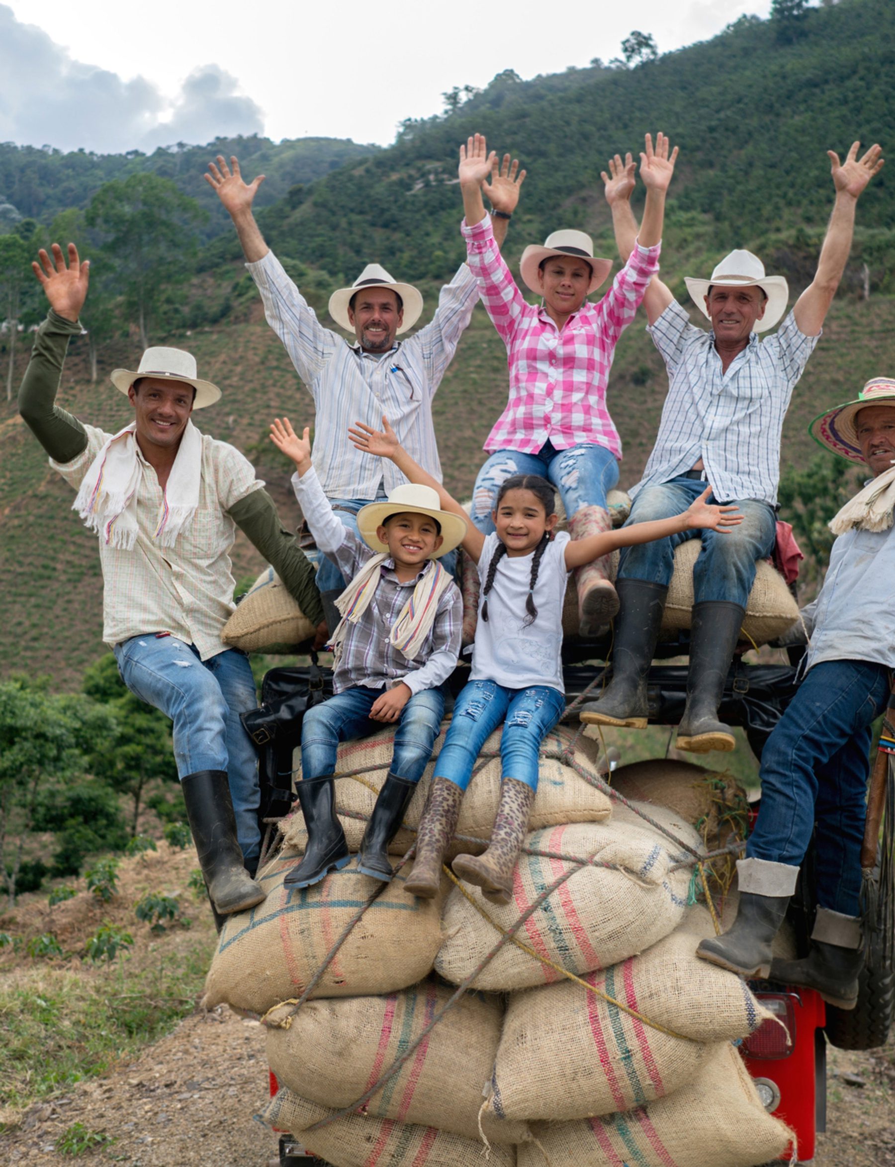 a group of farmers and their kids celebrating on top of bags of crops