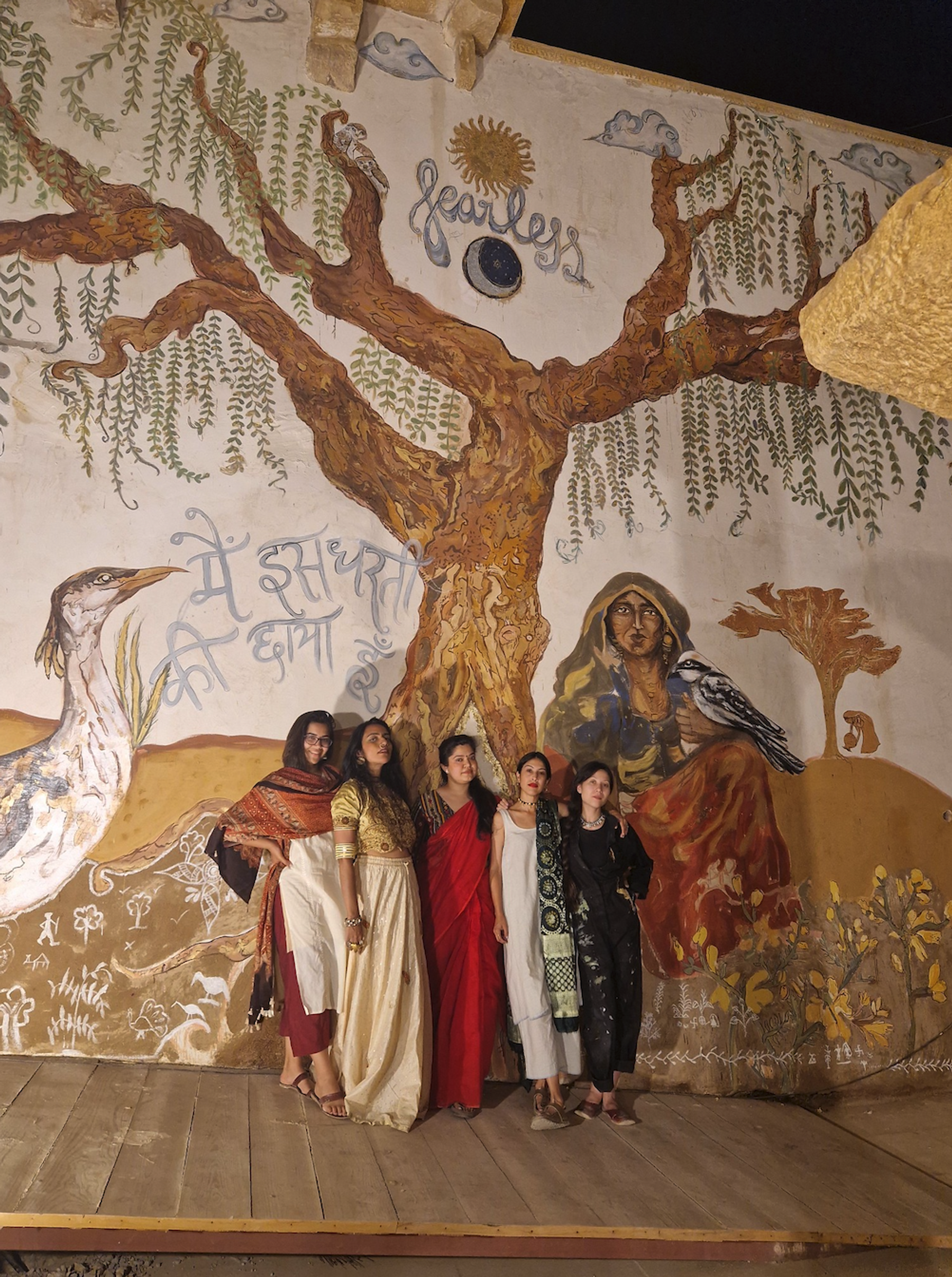 5 women stand in front of a large hand painted mural